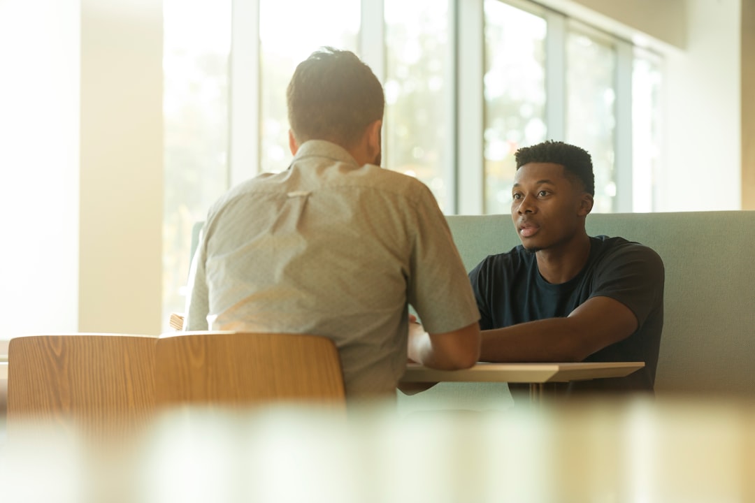 Two men sitting across a table in a bright room having a calm one-to-one conversation