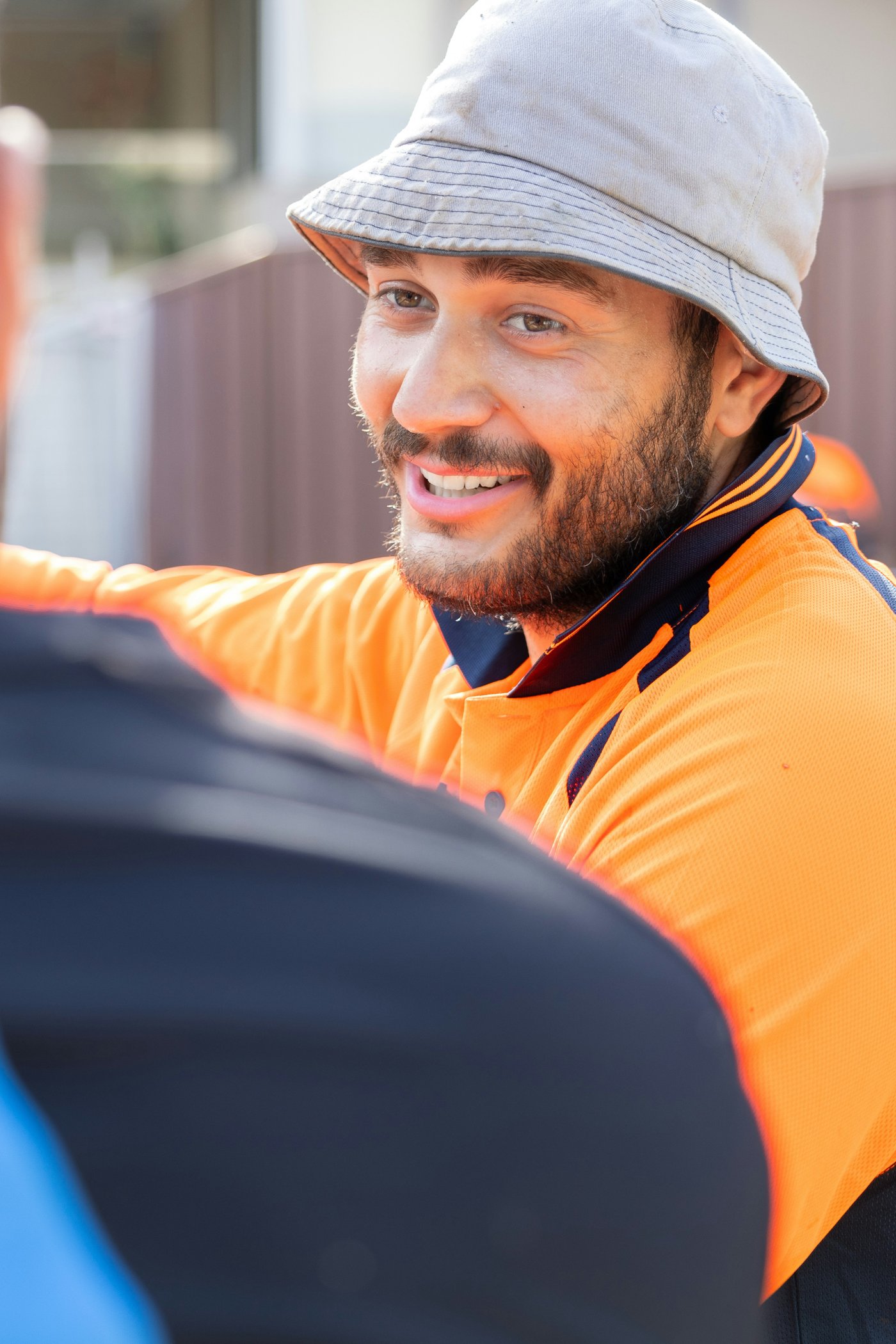 Tradesman in a hi-vis shirt and bucket hat smiling during a conversation outside a regional Australian home