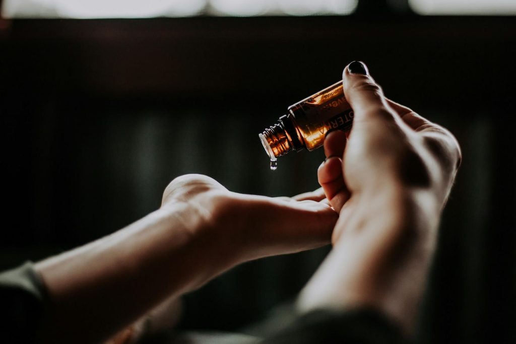 A person holding a small amber bottle, pouring a drop of liquid onto their other hand.