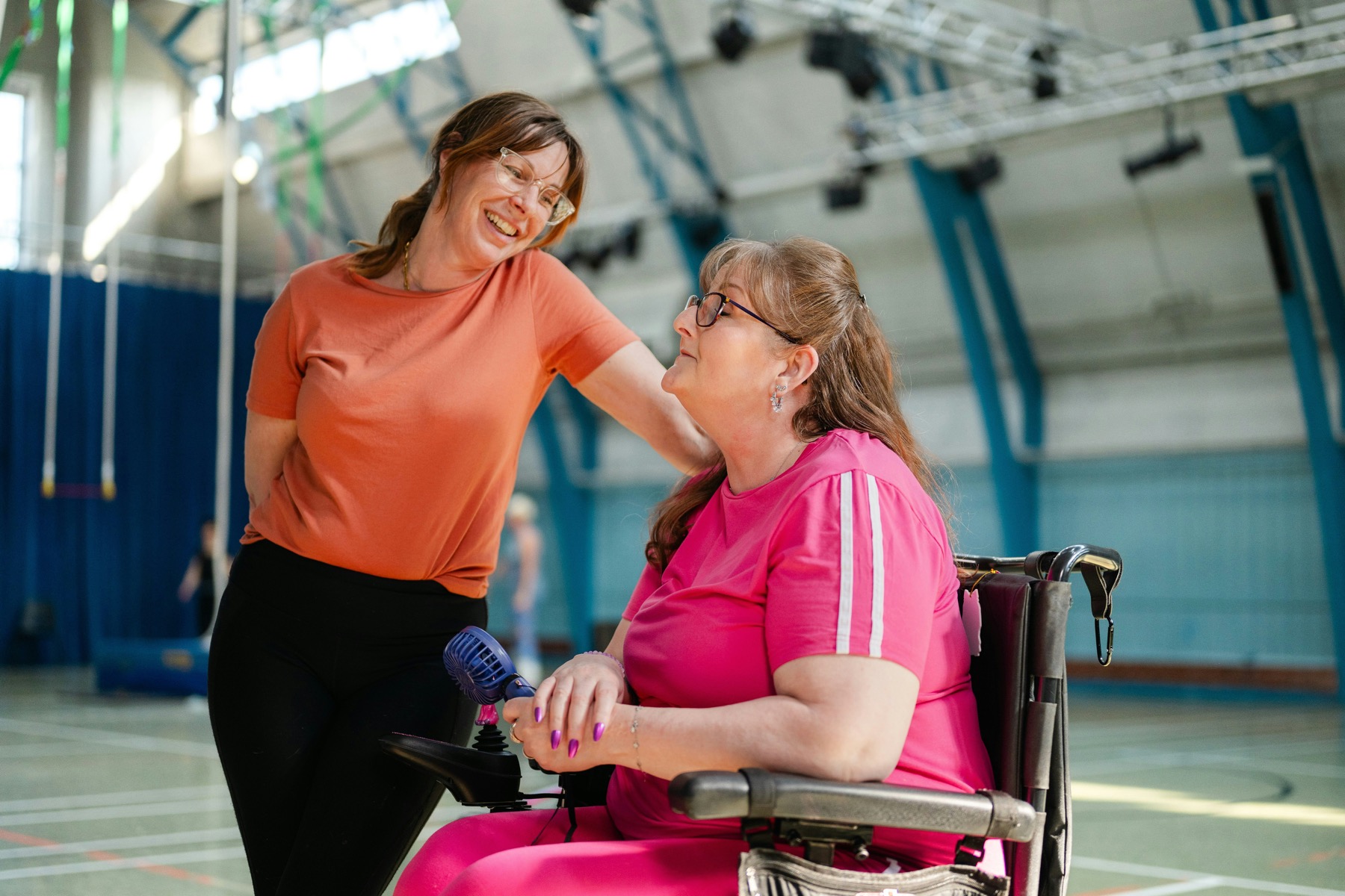 Support worker sharing a laugh with a woman using a power wheelchair at a community sports centre